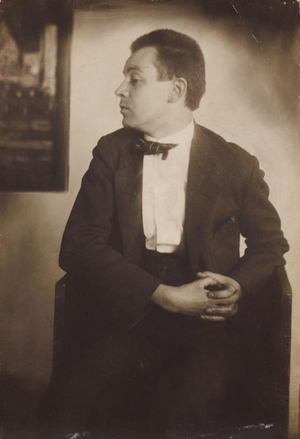 Egon Schiele im Profil, im Hintergrund das Gemälde Häuser am Meer 