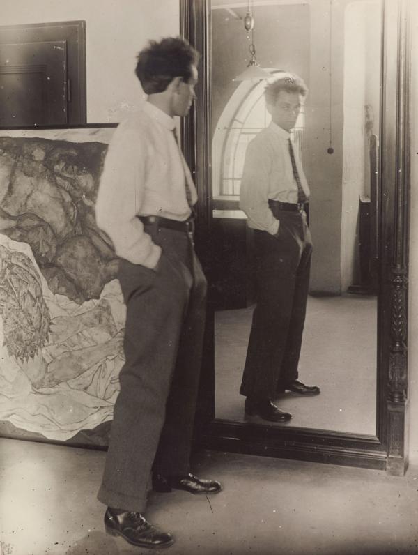 Egon Schiele vor dem Spiegel im Hietzinger Atelier, im Hintergrund das Gemälde Tod und Mädchen (Mann und Mädchen) 