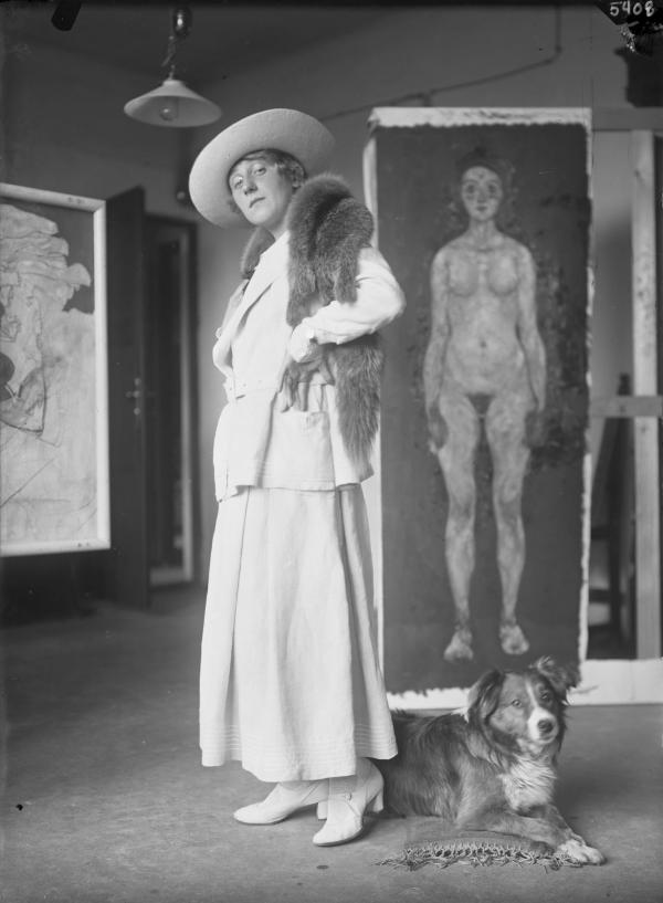 Edith Schiele mit ihrem Hund Lord, vor dem Gemälde Mädchen 
