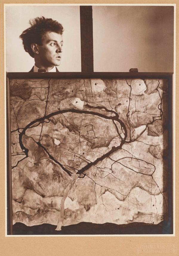 Egon Schiele hinter seinem auf einer Staffelei befindlichen Gemälde Herbstbaum in bewegter Luft (Winterbaum) 